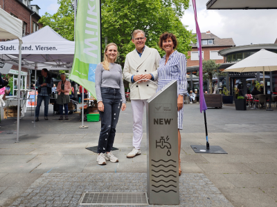 3 Personen hinter Trinkwasserbrunnen